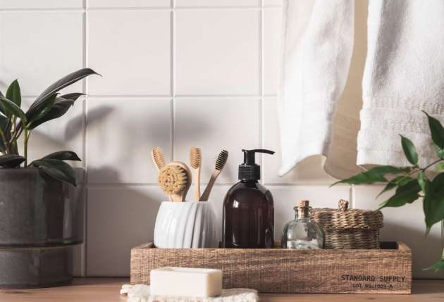 White bath background front view with cosmetic bottle, bath accessories, toothbrushes in a glass and houseplants on wood shelf and wall tiles. Front view. Copy space